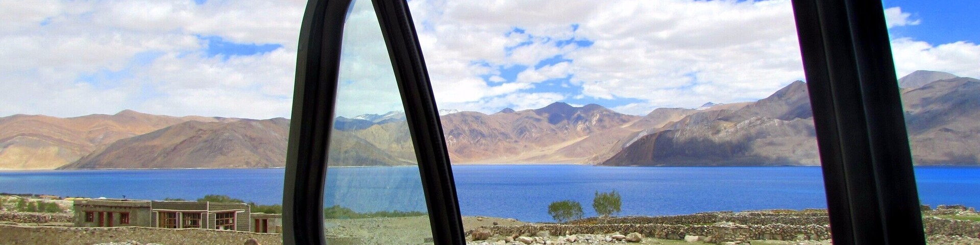 Ventana lateral de un coche con vistas a un lago, montañas y un cielo despejado.
