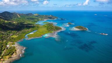 Vista aérea de una región costera con colinas verdes exuberantes, aguas azules cristalinas y pequeñas islas.