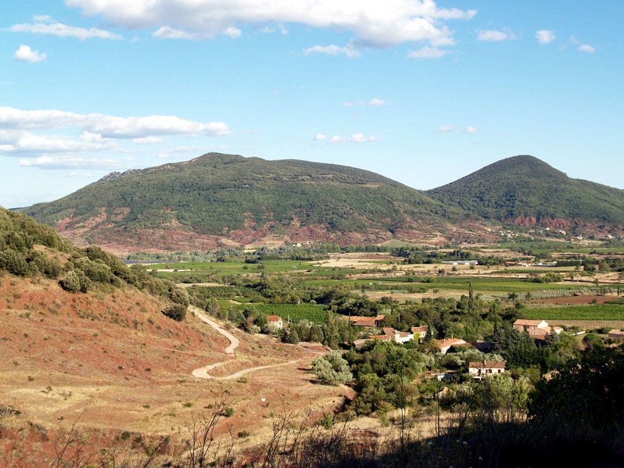 A rural landscape with rolling hills, a winding road, and scattered houses.