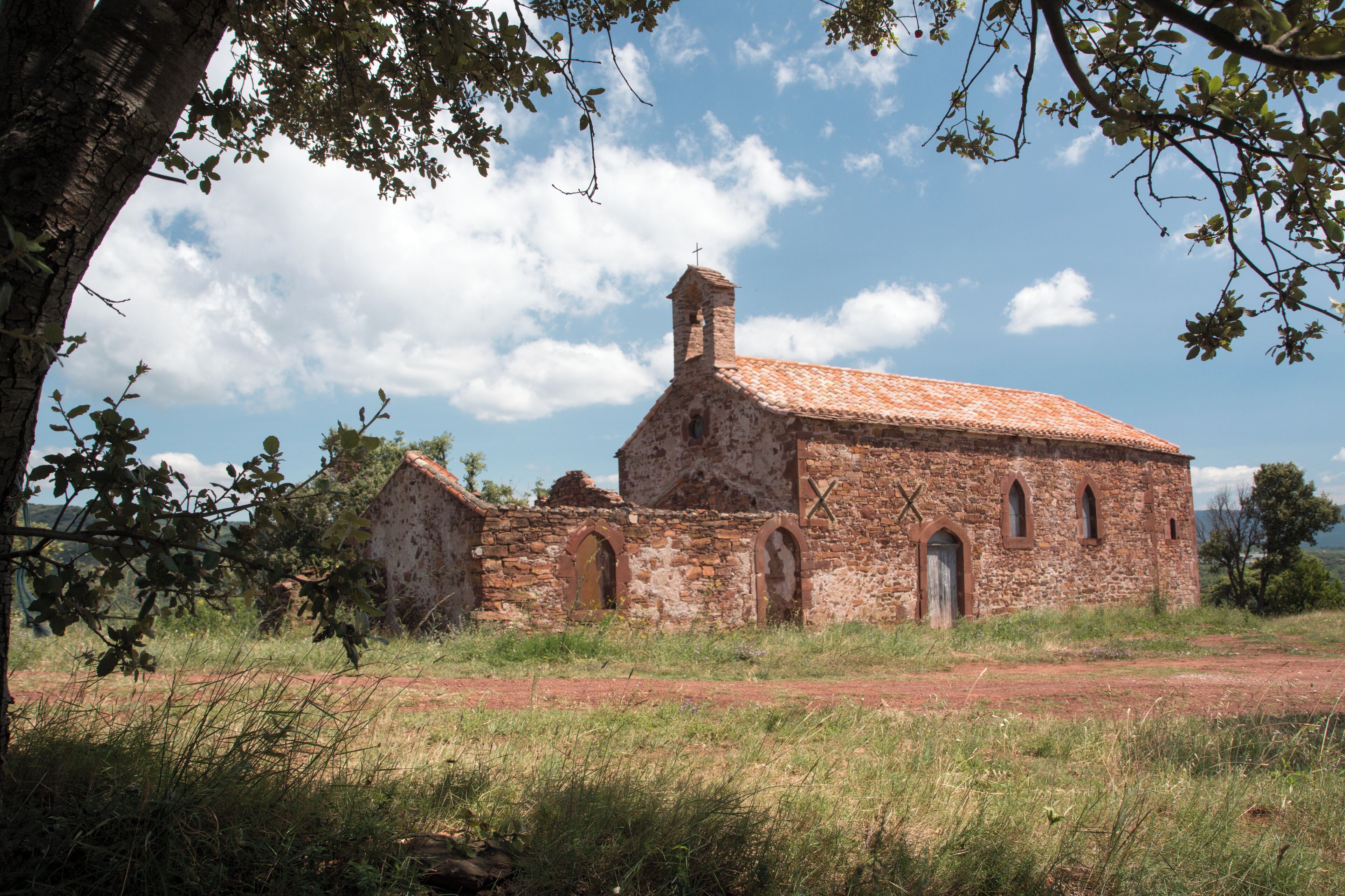 An old stone church with a cross on top, surrounded by grass and trees.