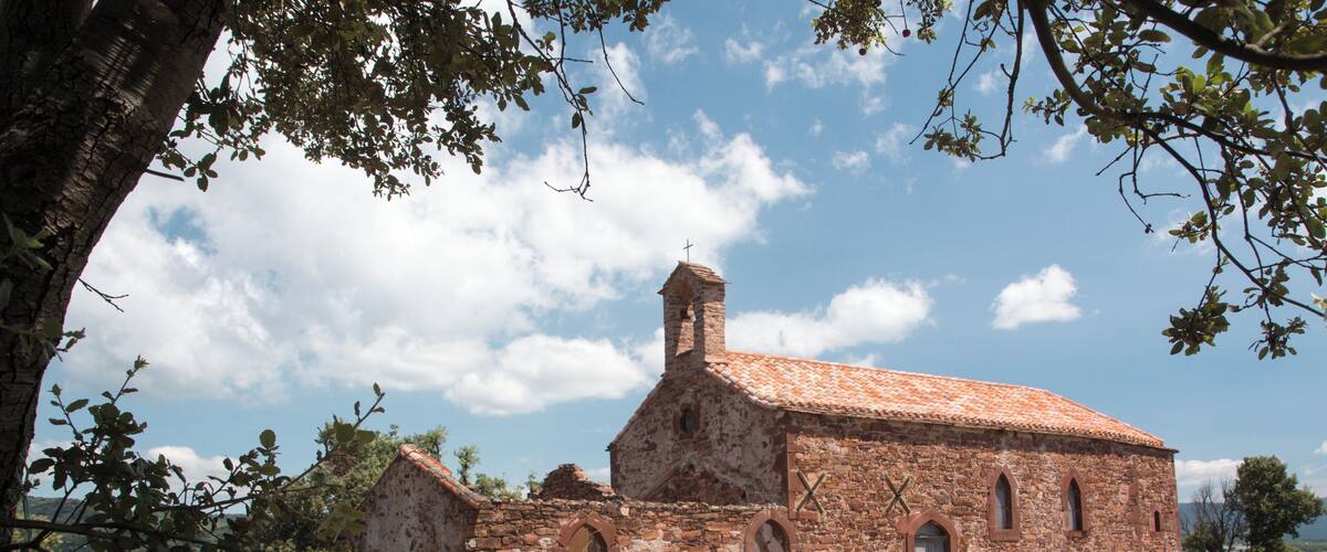 An old stone church with a cross on top, surrounded by grass and trees.