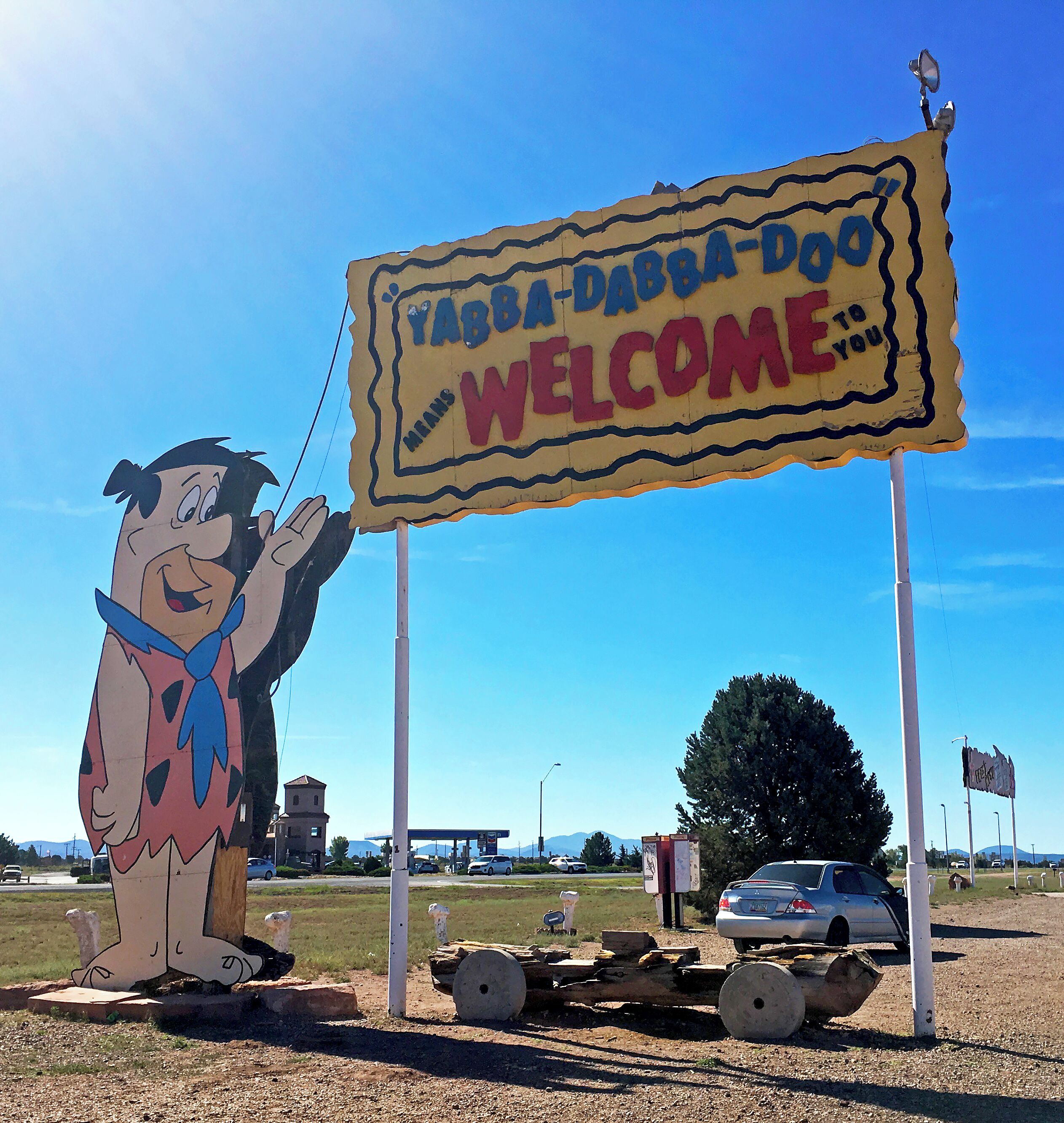 A cartoon character waving at a 'Yabba-Dabba-Doo Welcome' sign.