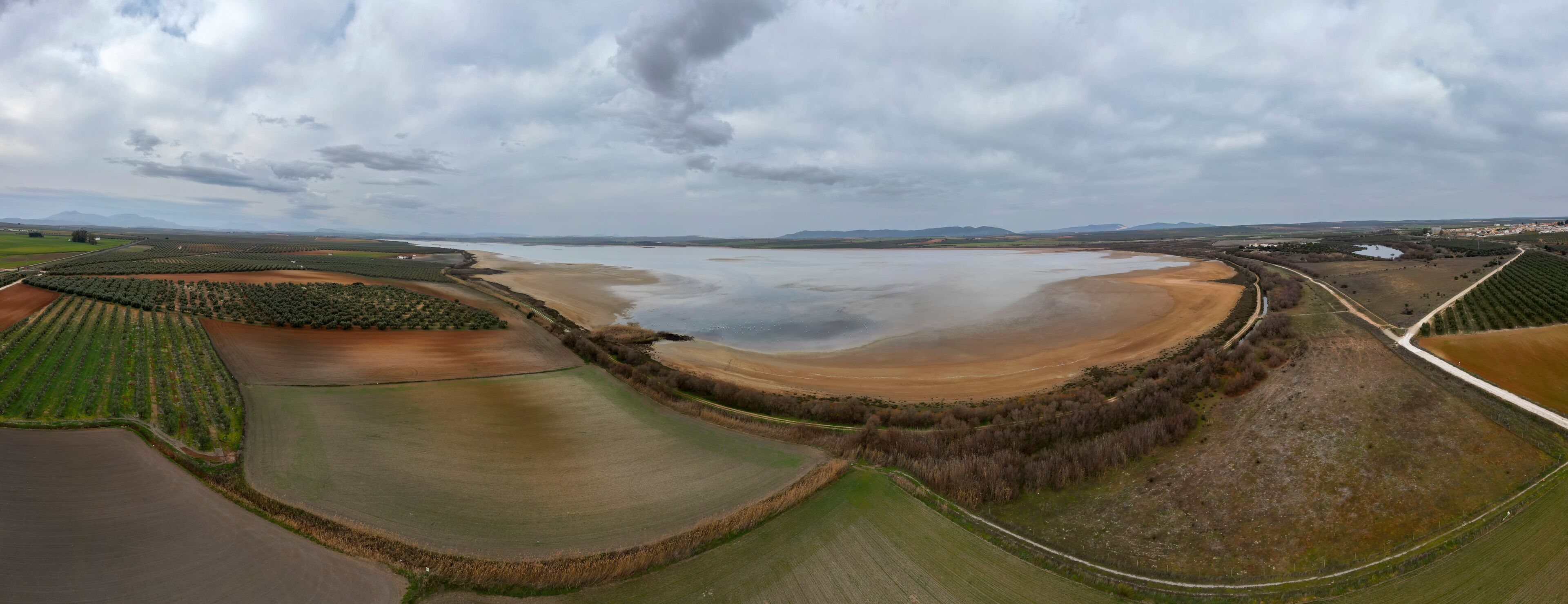 An aerial view of a coastal landscape with fields, a large body of water, and distant mountains.