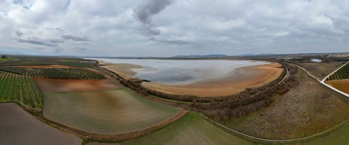 An aerial view of a coastal landscape with fields, a large body of water, and distant mountains.