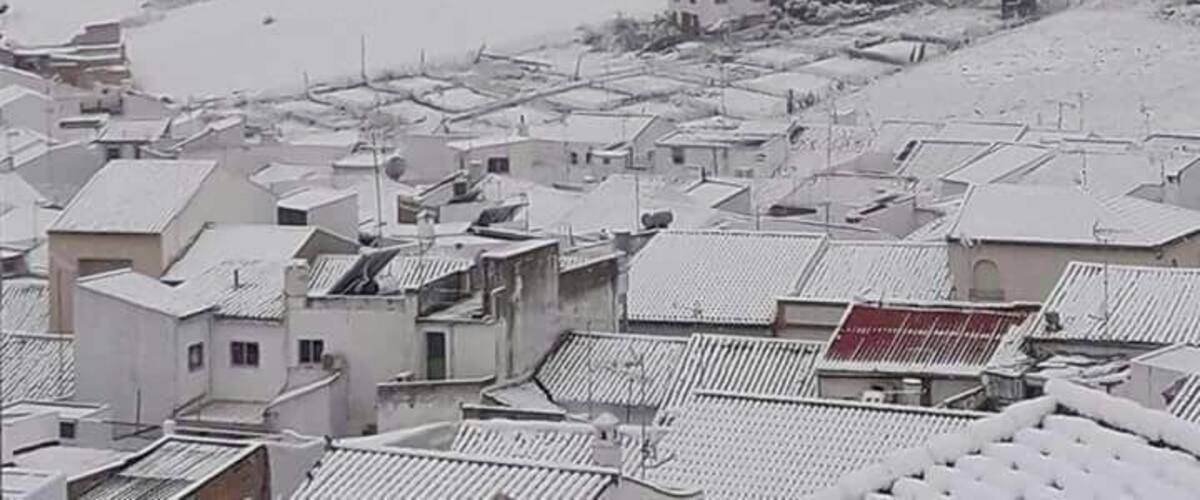 A snow-covered mountain with a small building on its peak and a residential area in the foreground.