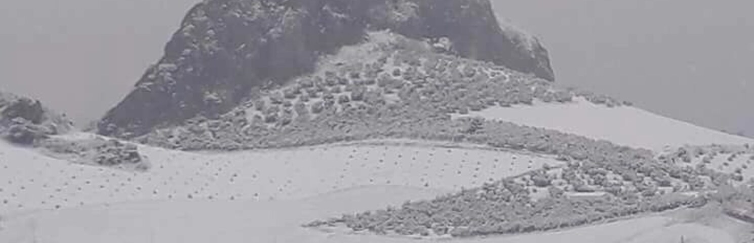 A snow-covered mountain with a small building on its peak and a residential area in the foreground.