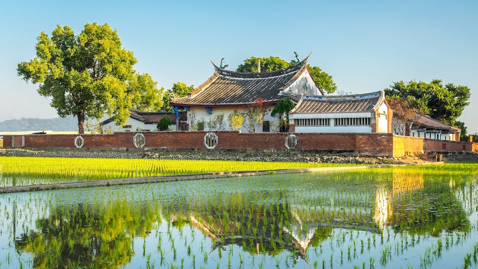 A traditional building with a tiled roof and brick walls, surrounded by a water body reflecting the structure.