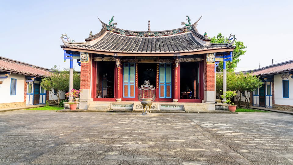 A traditional Chinese building with a tiled roof, red and blue doors, and a large stone lantern in front.