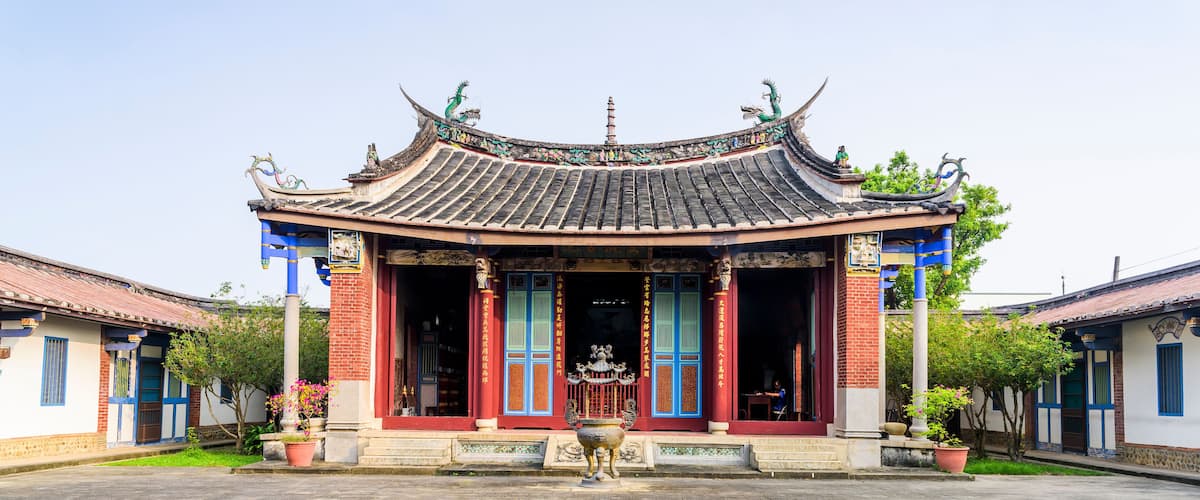 A traditional Chinese building with a tiled roof, red and blue doors, and a large stone lantern in front.