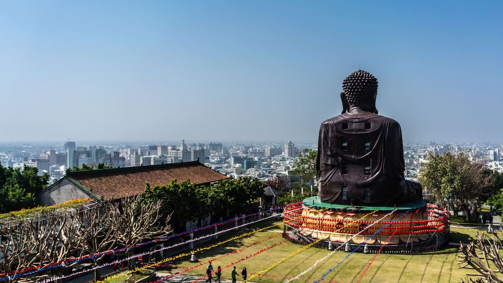 A large Buddha statue surrounded by colorful decorations, with a cityscape in the background.