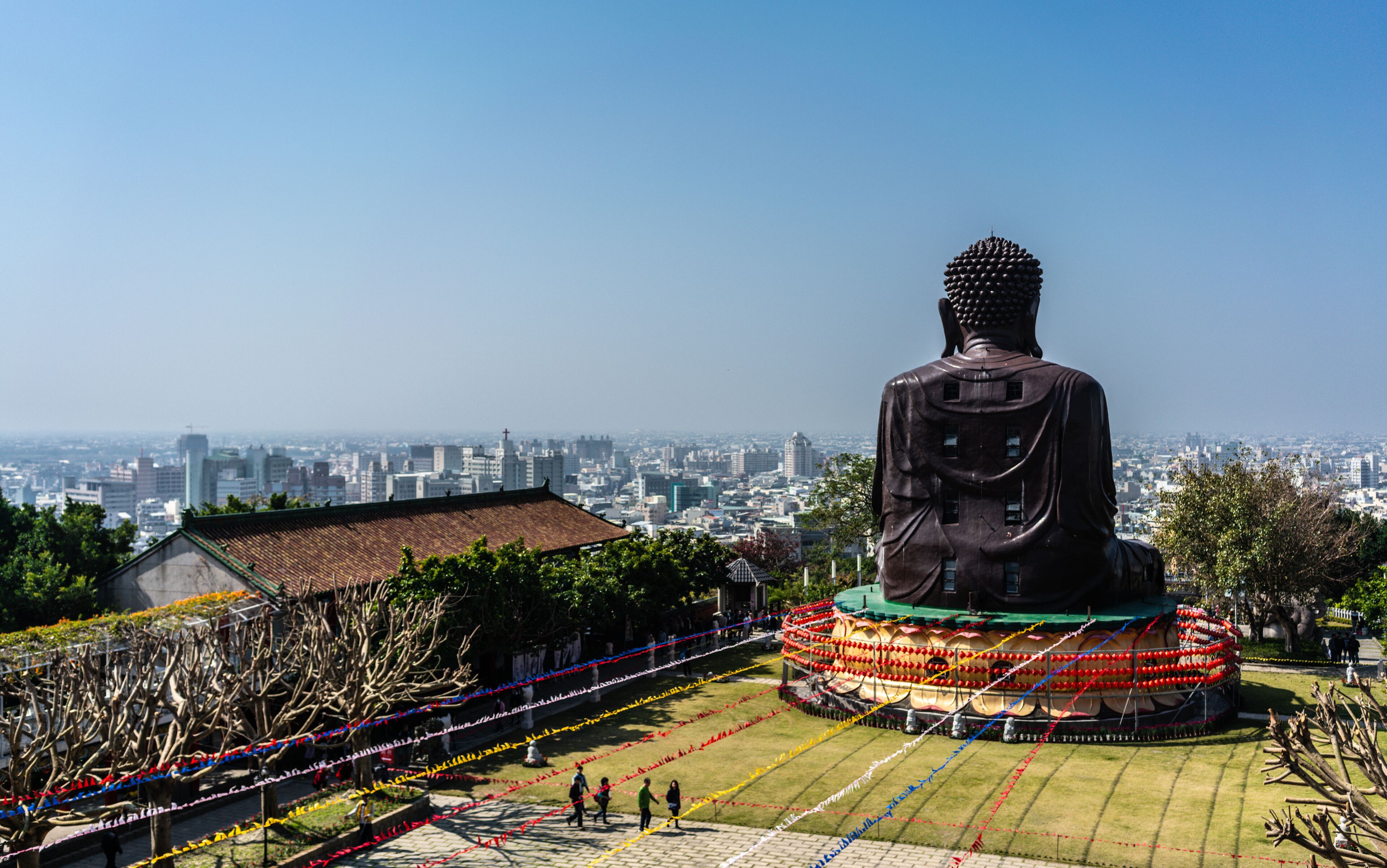 A large Buddha statue surrounded by colorful decorations, with a cityscape in the background.