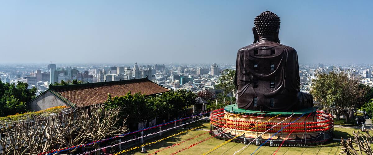 A large Buddha statue surrounded by colorful decorations, with a cityscape in the background.
