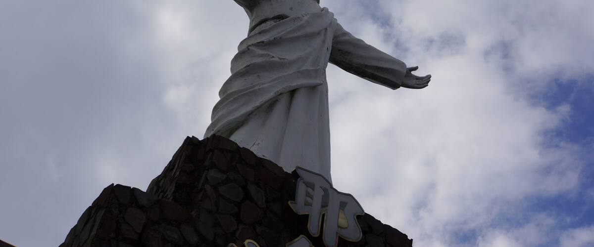A statue with outstretched arms on a rocky pedestal against a cloudy sky.