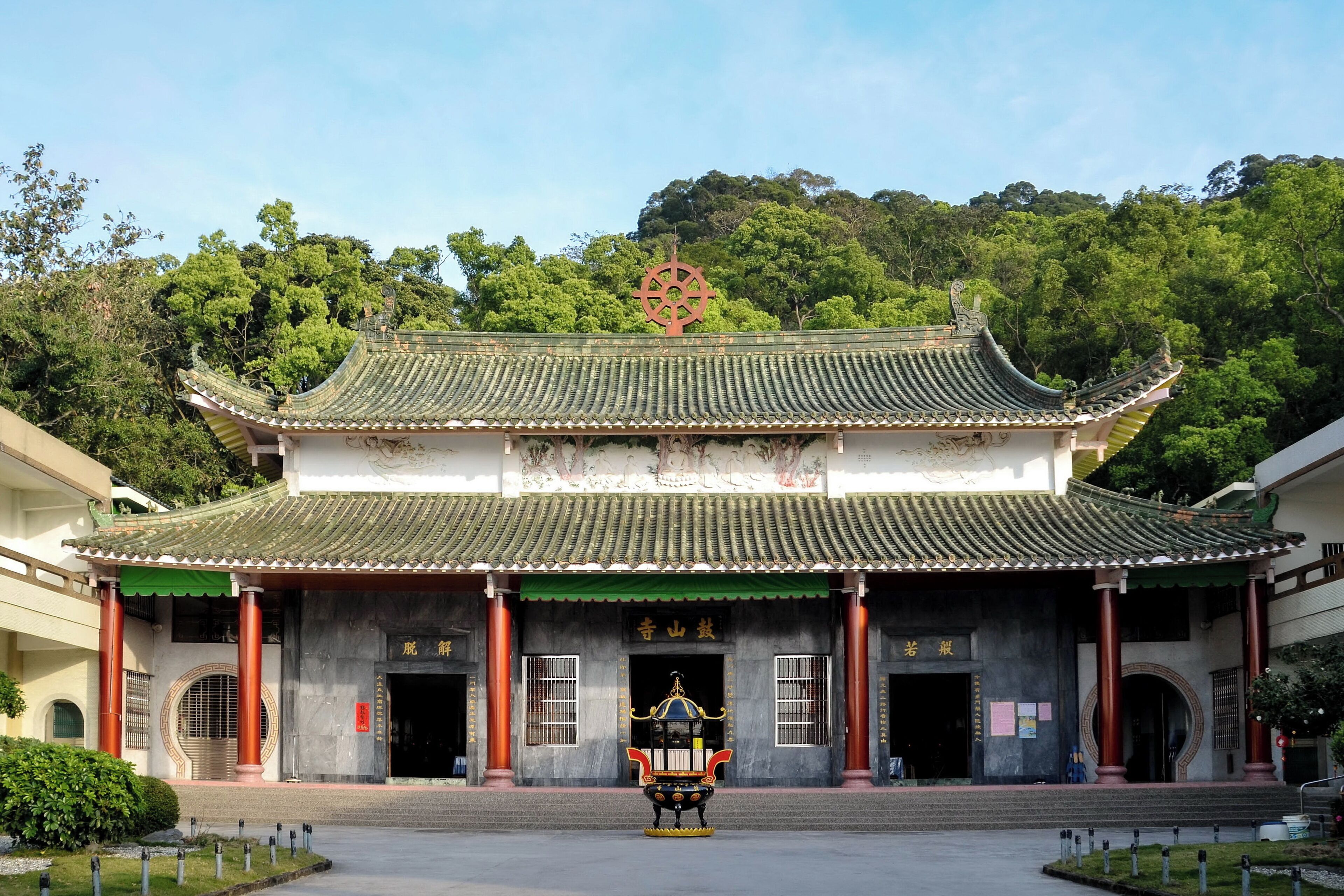 A traditional Chinese building with a green-tiled roof, a large red emblem, and a statue in front.