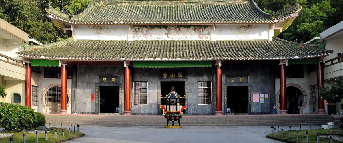A traditional Chinese building with a green-tiled roof, a large red emblem, and a statue in front.