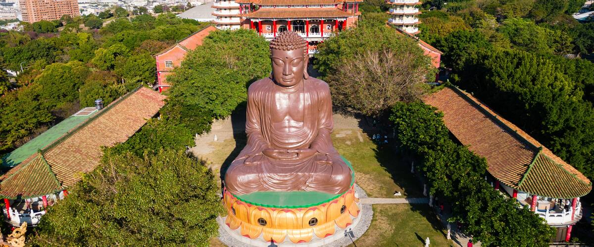 A large Buddha statue surrounded by traditional buildings and greenery.