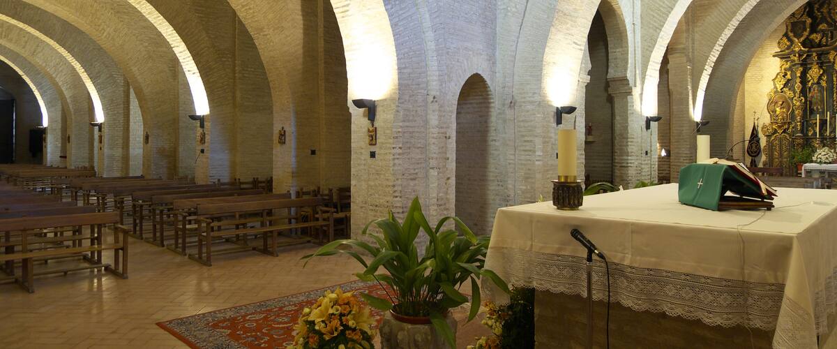 An interior of a church with arched ceilings, wooden pews, a podium, and a large crucifix.