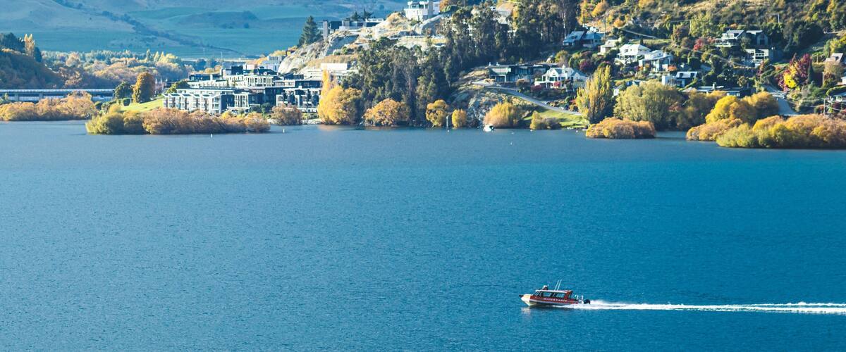 A lake with a boat, houses on a hillside, and autumn trees.