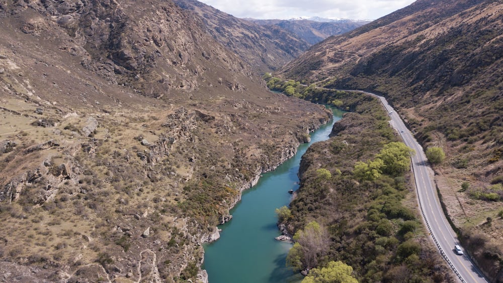 A winding river through a mountainous landscape with a road alongside it.