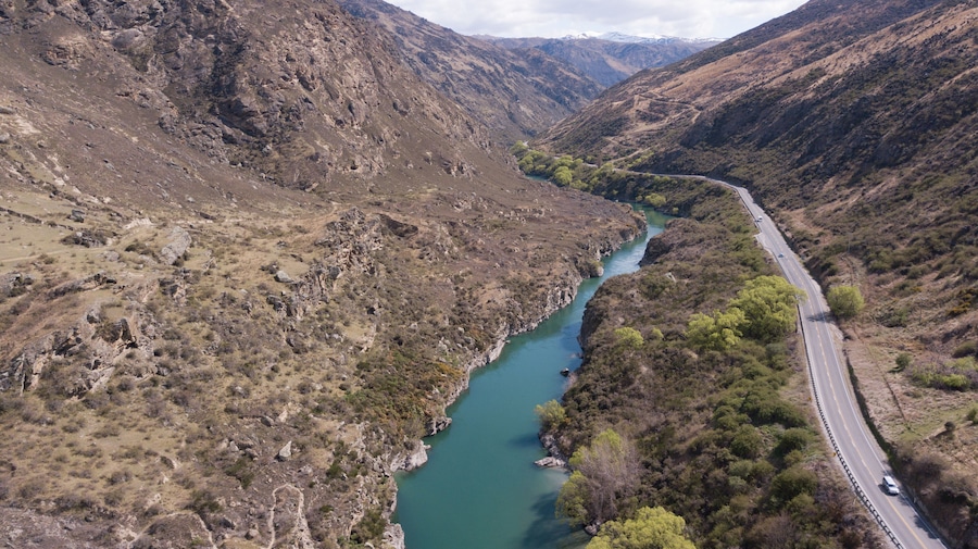 Un río sinuoso atraviesa un paisaje montañoso con una carretera que lo acompaña.