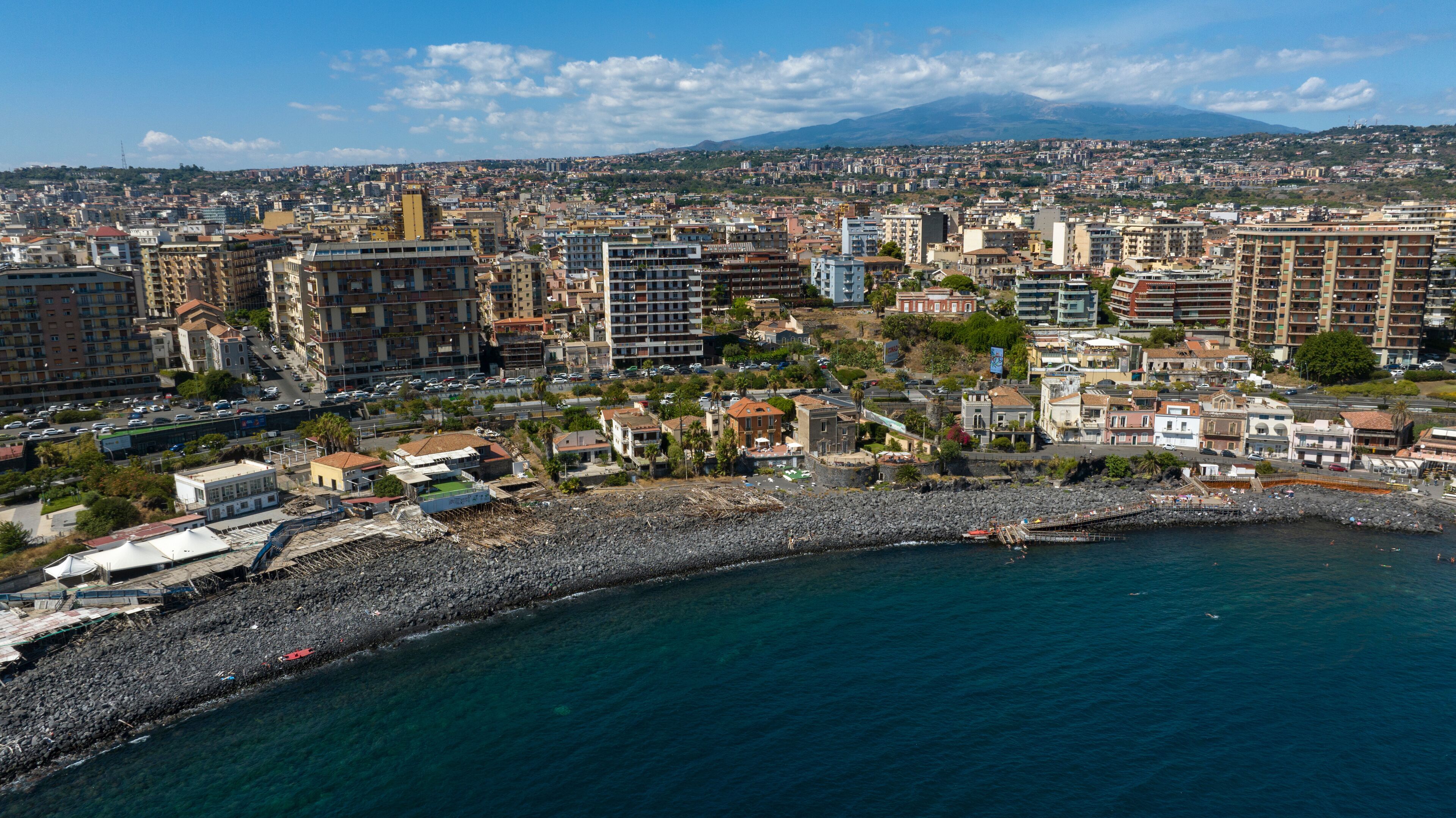 Aerial view of San Giovanni li Cuti beach. It is a small seaside village in the eastern part of the city of Catania, Sicily, Italy. In the background, on the horizon, is Mount Etna in silhouette.