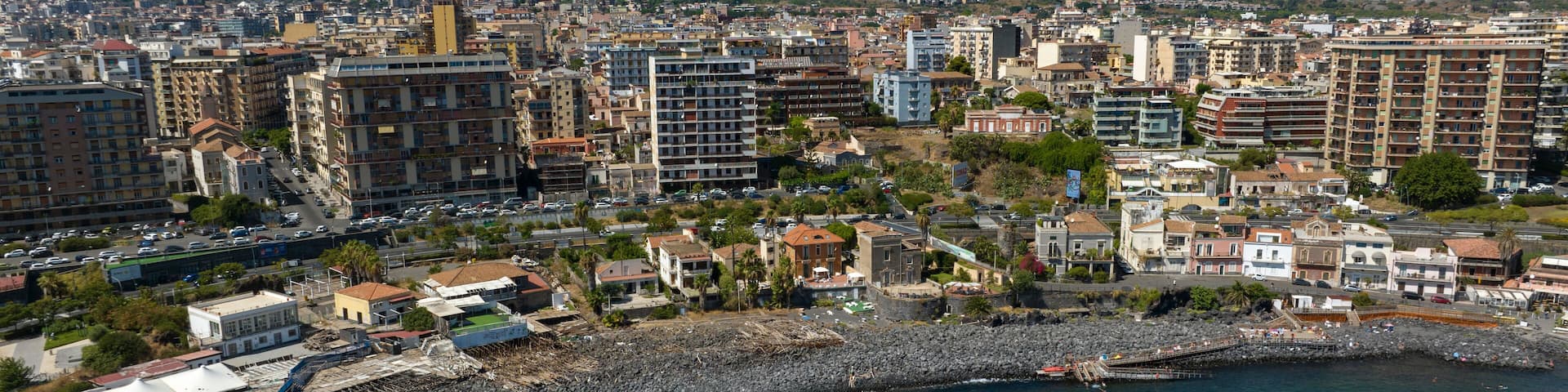 Aerial view of San Giovanni li Cuti beach. It is a small seaside village in the eastern part of the city of Catania, Sicily, Italy. In the background, on the horizon, is Mount Etna in silhouette.