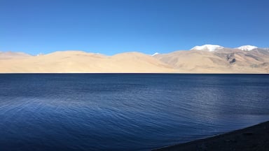 Un lac paisible, sous un ciel bleu dégagé, avec des montagnes enneigées à l’horizon.