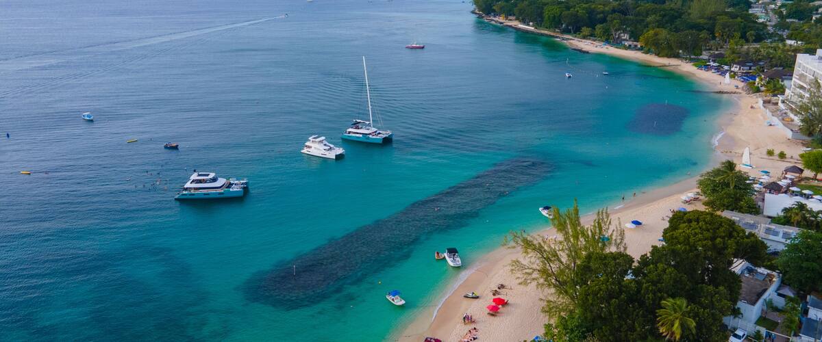 A coastal area with clear turquoise waters, a sandy beach, and several boats anchored near the shore.