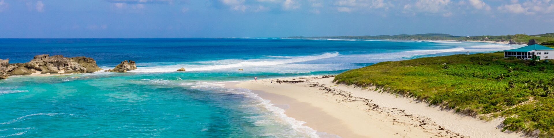 Uma praia com águas azul-turquesa, areal arenoso e um edifício branco à direita.