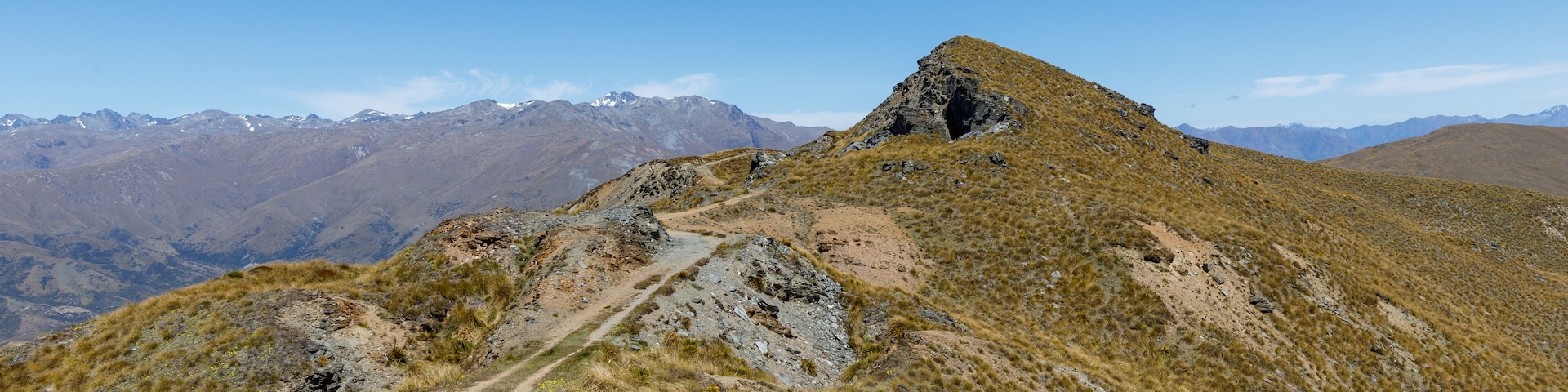 Sendero de montaña que conduce a un pico rocoso bajo un cielo azul despejado.