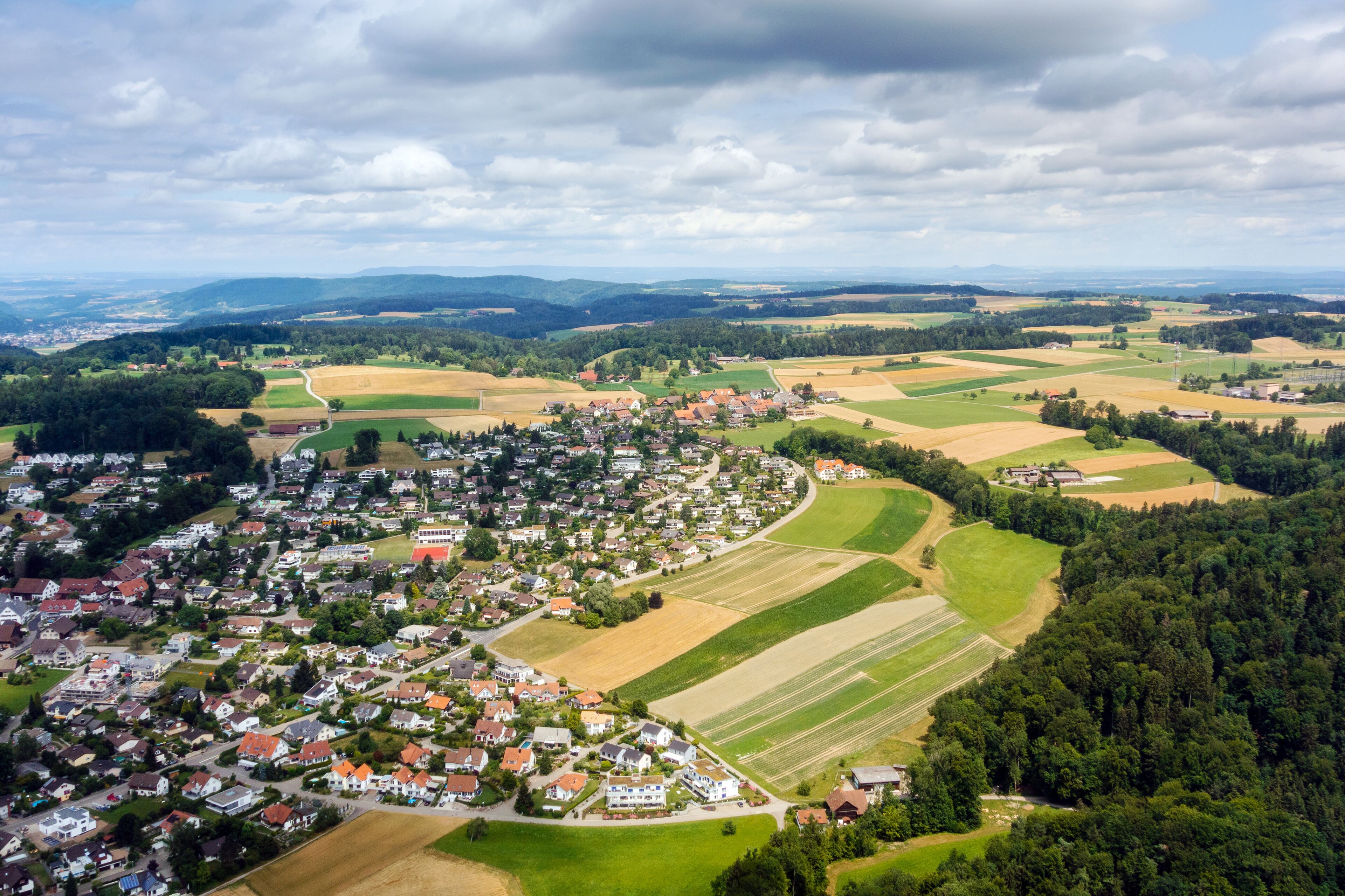 A rural landscape with a small village, fields, and distant mountains.