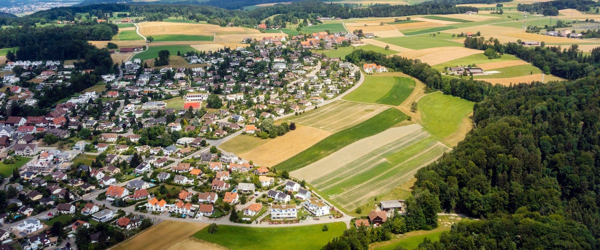 A rural landscape with a small village, fields, and distant mountains.