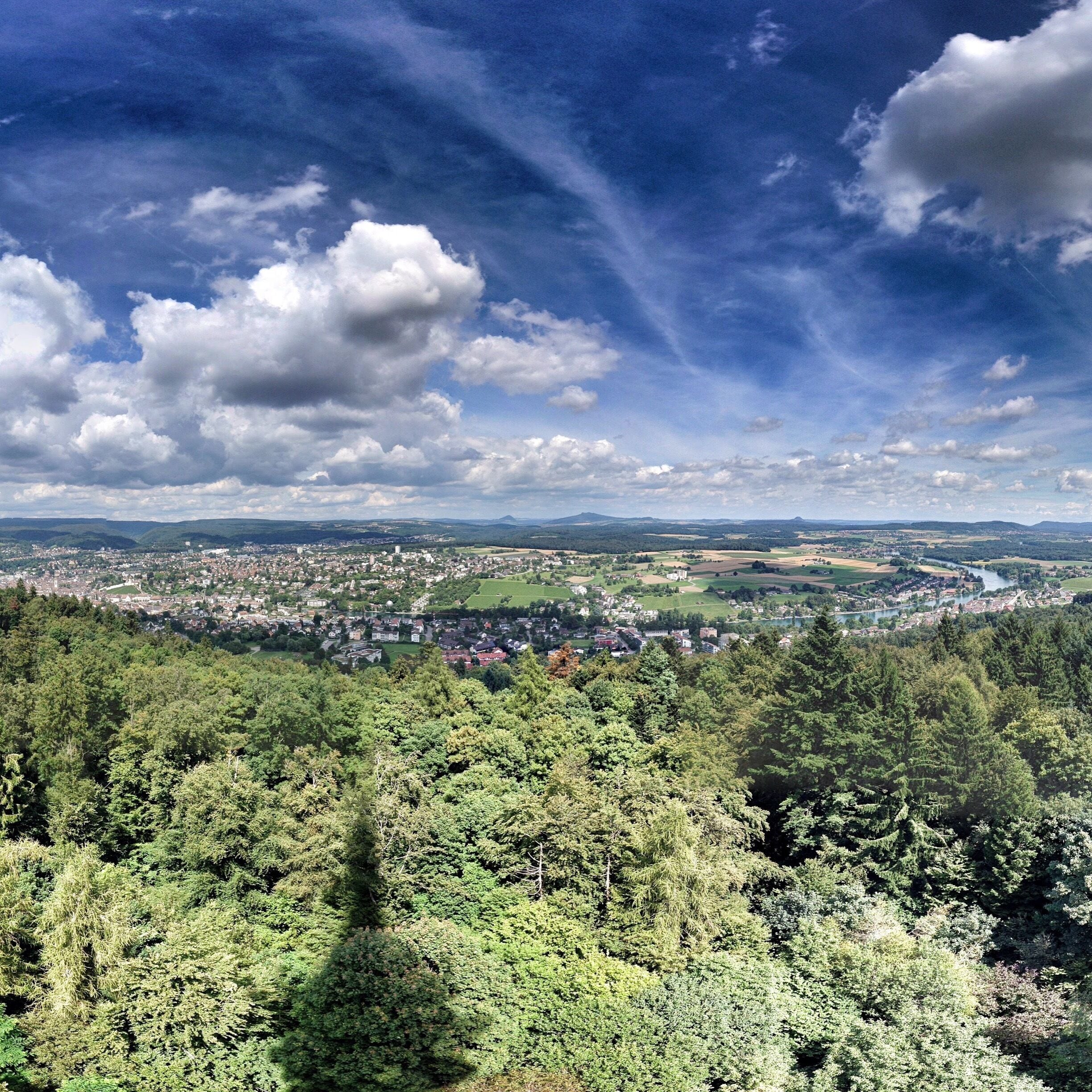 A panoramic view of a town nestled in a valley with dense forests in the foreground and a river running through the town.