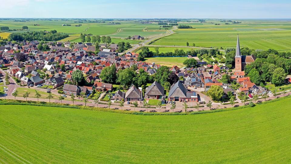 An aerial view of a village with red-roofed houses, a church, and surrounding green fields.