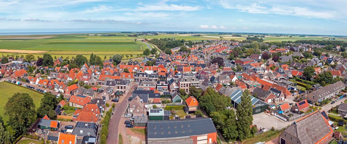 An aerial view of a town with red-roofed houses, a church with a tall steeple, and expansive green fields in the background.