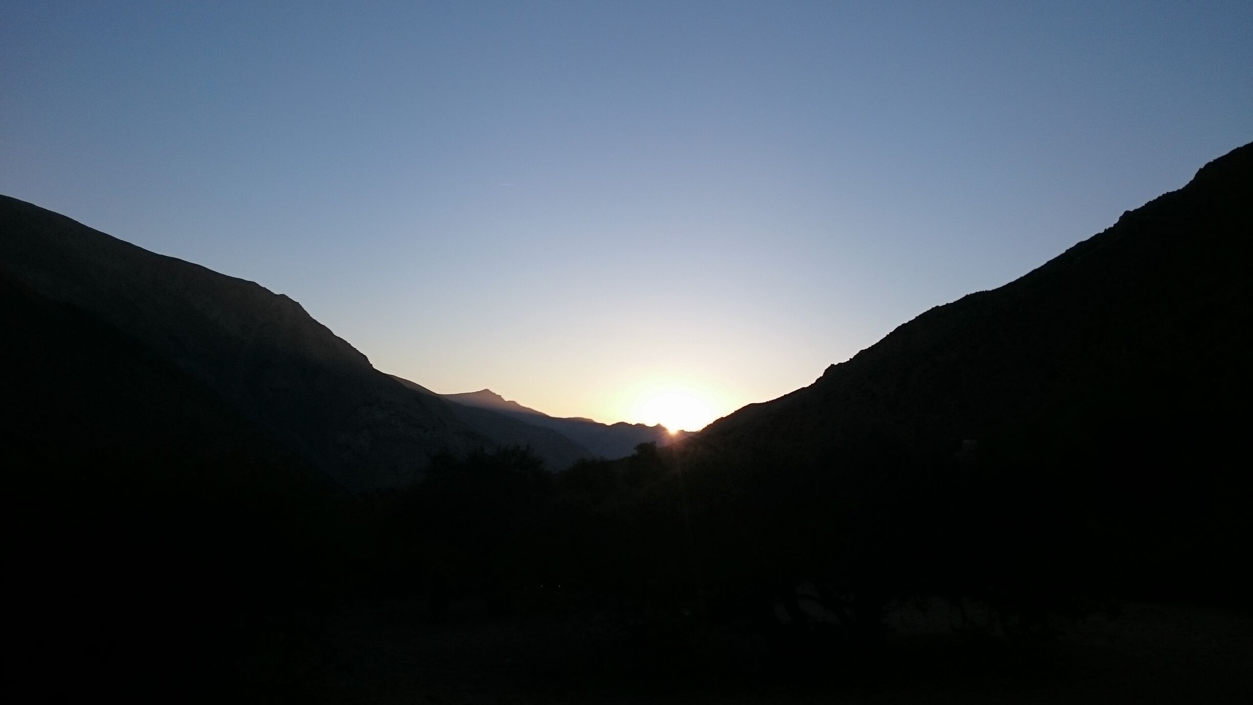 A mountain landscape with a sun setting between two peaks.