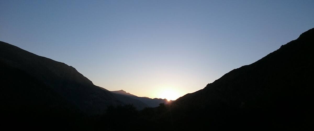 A mountain landscape with a sun setting between two peaks.