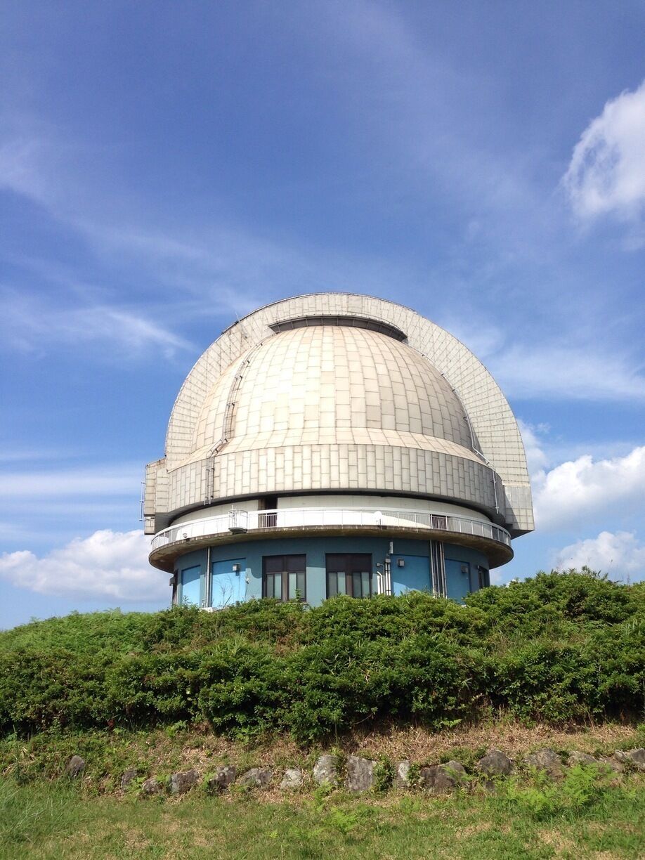 A large observatory dome with a blue base, surrounded by greenery and under a clear sky.
