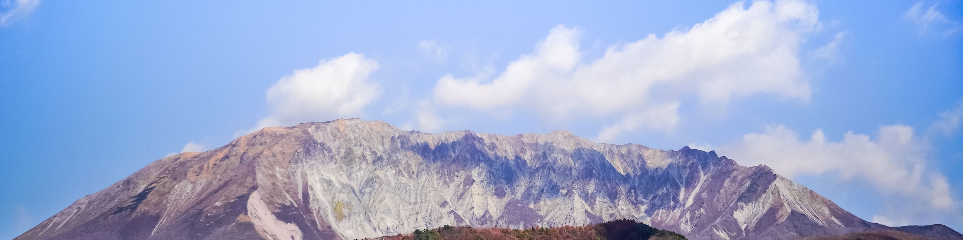 Ein Berg mit blauem Himmel, herbstlich gefärbten Bäumen und einem dichten Wald am Fuße.