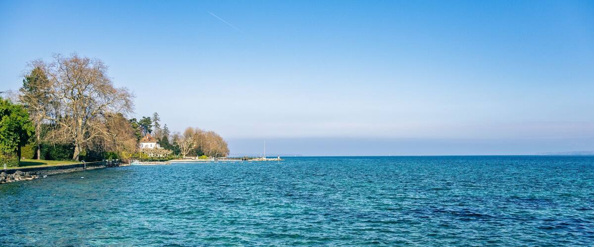 A clear blue sea with a pier, trees, and a white building on the shore.