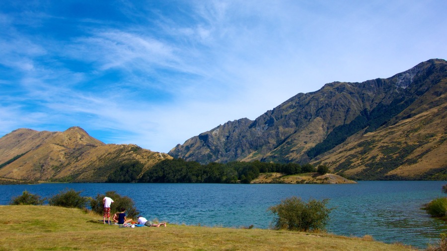 A lake surrounded by mountains, with people relaxing on the shore.