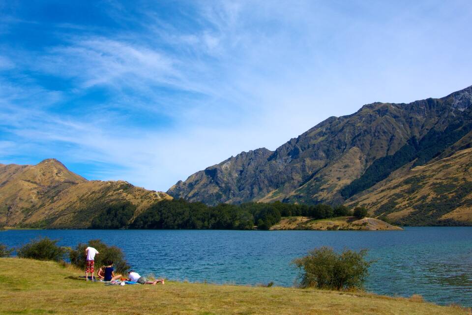 A lake surrounded by mountains, with people relaxing on the shore.
