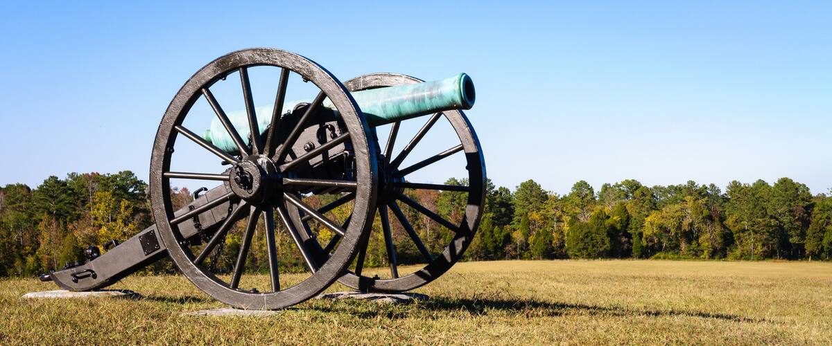 A cannon in a grassy field with trees in the background.