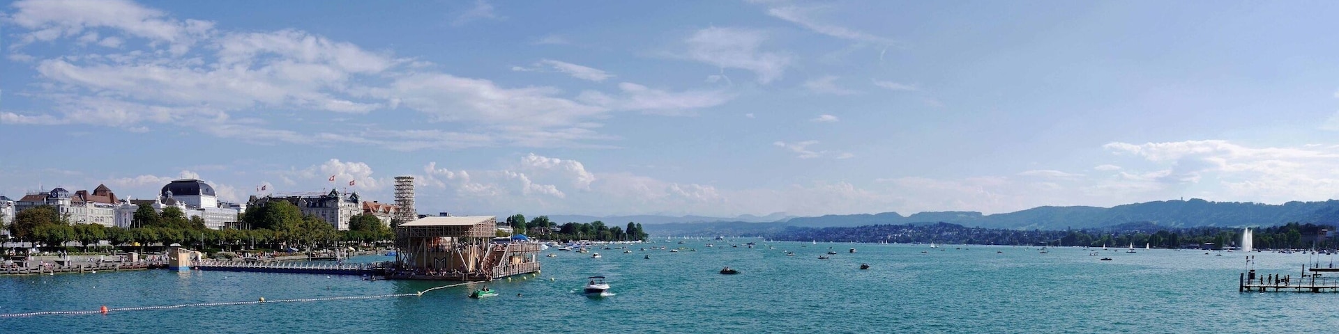 A panorama of the stunning Lake Zurich from the Quaibrucke Bridge. On a lovely summer's day there is a lot of activity on the Lake including a wooden lido with rest areas and cafe/bar.