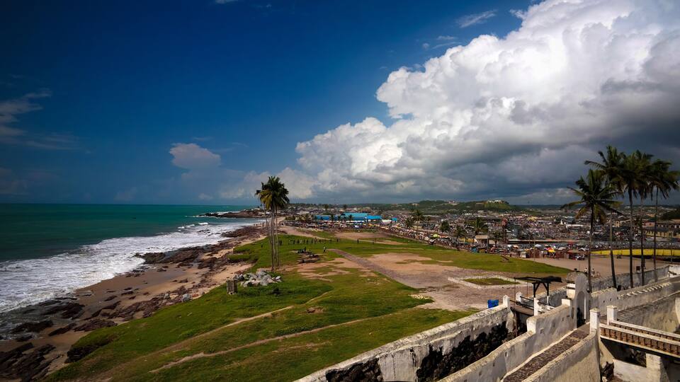 A coastal cityscape with a beach, palm trees, and a large cloud formation.