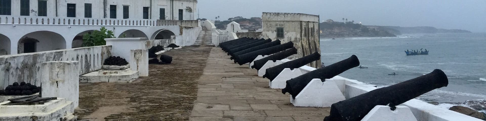 A coastal fort with cannons lined up along a walkway, overlooking the sea.