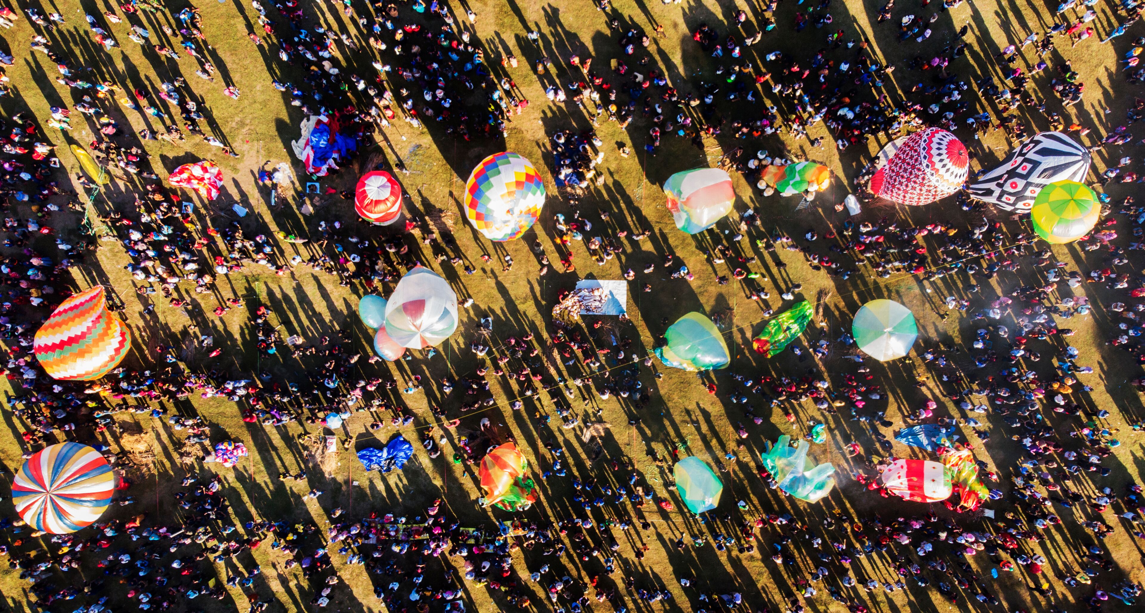 An aerial view of a crowded festival with numerous colorful balloons and people.