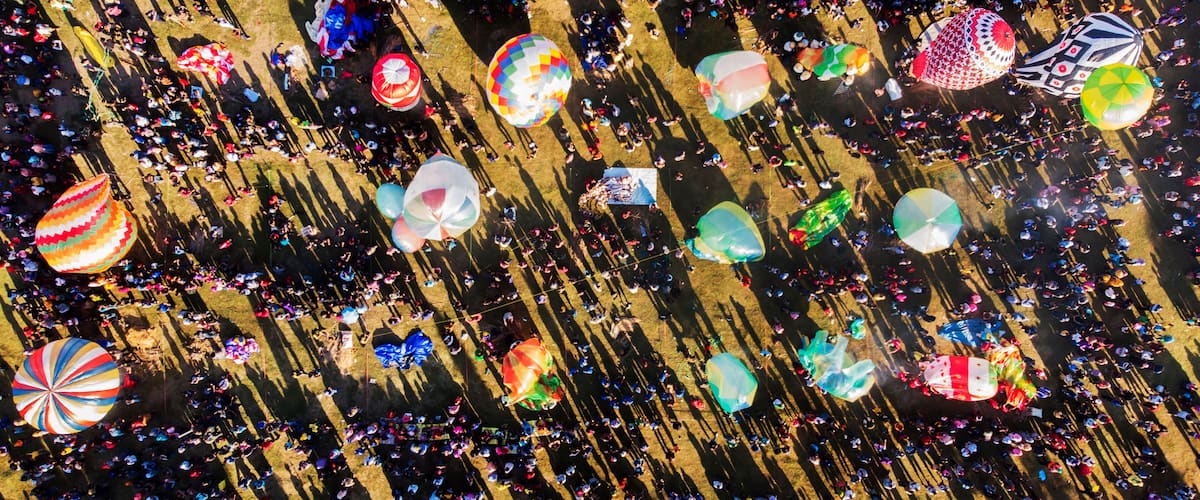 An aerial view of a crowded festival with numerous colorful balloons and people.
