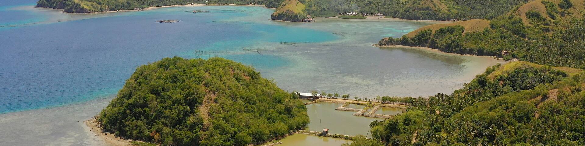 A coastal landscape with clear turquoise waters, green hills, and a small island with a dock.