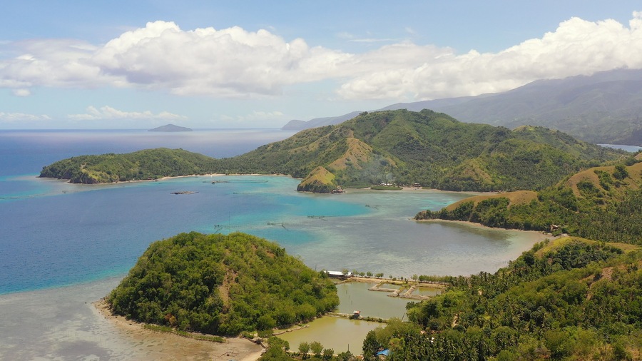 Un paisaje costero con aguas turquesas cristalinas, colinas verdes y una pequeña isla con un muelle.